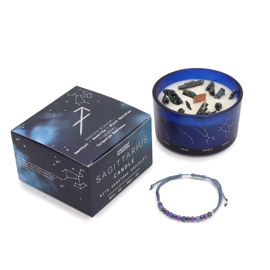 A blue candle decorated with gemstones sits beside a bracelet and box. The box reads: "SAGITTARIUS CANDLE WITH GEMSTONE BRACELET Nov. 22 - Dec. 21." Zodiac constellations are illustrated around the candle.