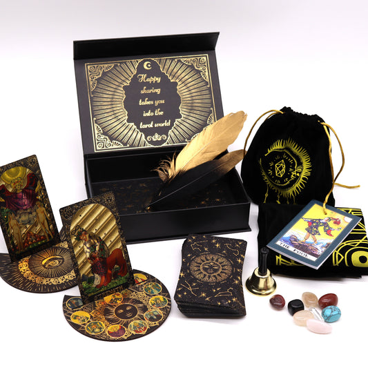 Tarot card set displayed with ornate cards, circular reading mats, a black box labeled "Happy sharing takes you into the tarot world," feathers, a drawstring bag, stones, and a small bell.