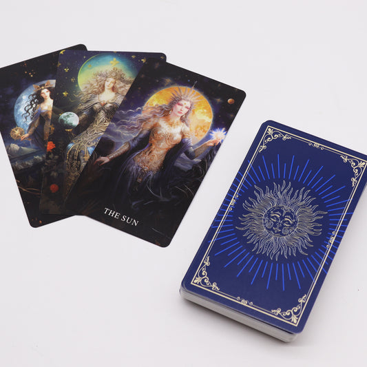 Three intricately designed tarot cards, with the top card labeled "THE SUN," are displayed beside a blue, silver-accented deck box featuring a radiant sun illustration, set against a plain surface.