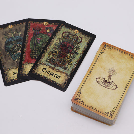 Three tarot cards with skull designs, named "Ace," "9," and "Emperor," are laid out. A nearby card deck features a skull and candle illustration, set on a plain surface.