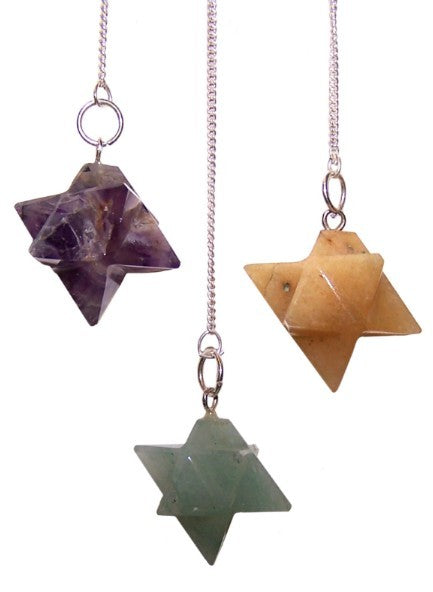 Three crystal pendants are suspended against a white background. The crystals are cut into star shapes, and each hangs from a silver chain attached to a small silver ring. The crystals are purple, tan, and green.