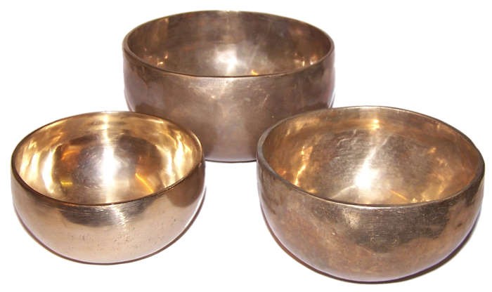 Three metallic bowls are displayed, varying in size and reflecting light. Arranged on a plain white background, the bowls have a polished, bronze-like appearance with a hammered texture.