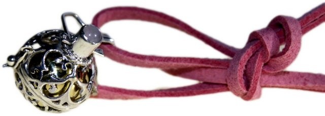 A silver filigree pendant hangs from a knotted mauve cord. The pendant has an opening on one side revealing a gold-colored sphere within.