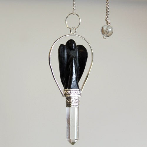A pendulum hangs, featuring a clear quartz point topped with a black angel sculpture cradled in silver, against a neutral background.