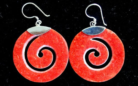 Two earrings hang against a dark background. Each earring is a flat, red circle with a carved spiral and a silver hook attached to the top.
