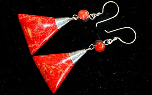 Earrings, made with triangle-shaped red coral stones, dangle from silver hooks in a dark setting.