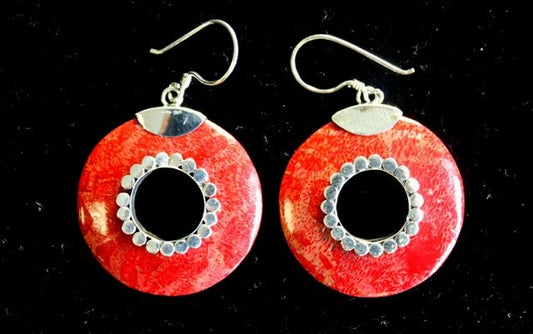 Two red coral-like earrings dangle against a black background. Each earring is round, hollow in the middle, and features silver-toned accents and hooks.