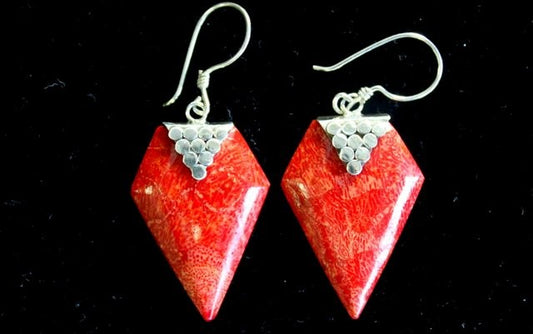 Two diamond-shaped coral earrings dangle against a dark background. Each has a silver triangular cap made of small round beads and silver ear hooks.