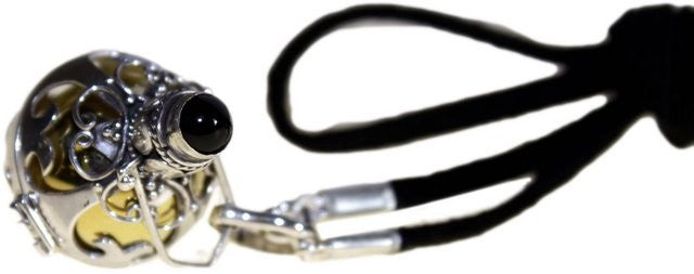 A silver pendant with a black stone rests with a yellow interior, attached to black cord with silver fittings against a white backdrop.