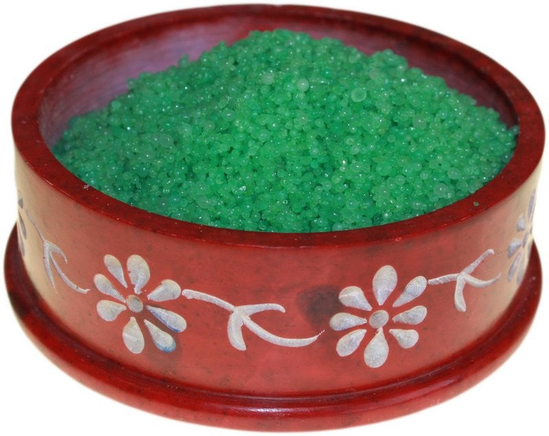 A red, circular container filled with green silica gel beads, decorated with white floral patterns, rests on a plain background.