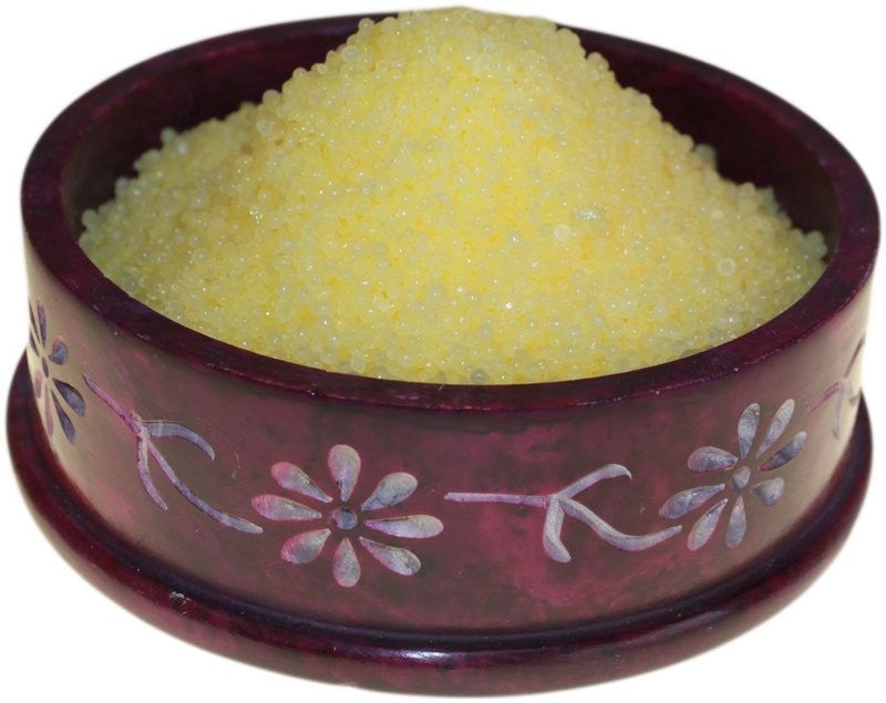 A round, decorative maroon bowl holds yellow granules, piled high. The bowl features floral patterns, providing an ornate context.