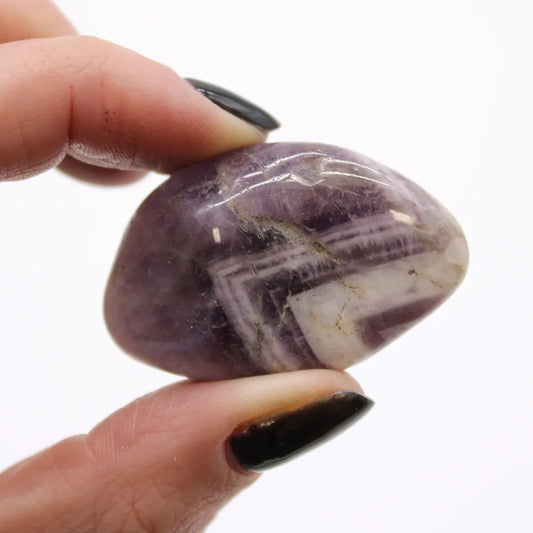 A polished, purple and white striped stone is being held between two fingers with black nail polish, set against a plain, white background.