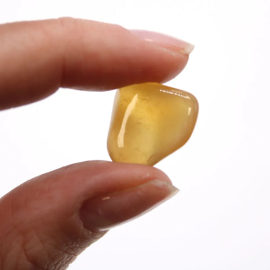 A yellow tumbled stone is held between a thumb and finger, with the white background.