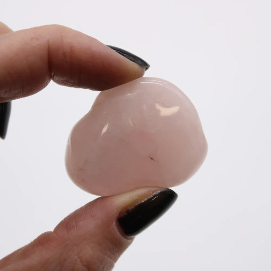 A hand with black nail polish holds a polished, light pink stone in front of a white background.