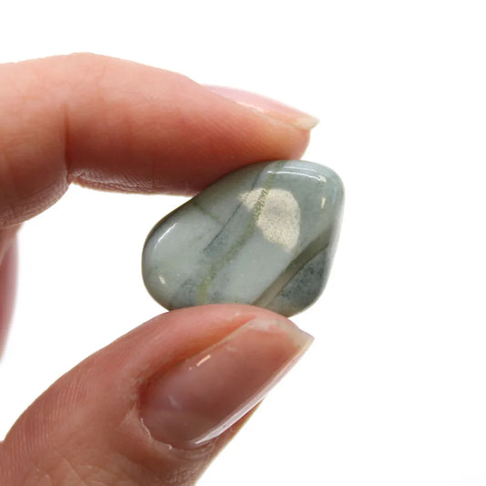 A polished, light blue-green stone with mineral banding is being held between a person's thumb and forefinger, against a plain white background.