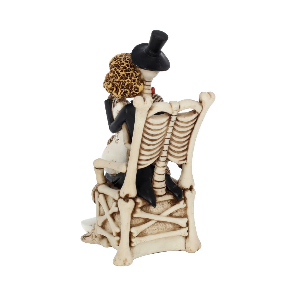 A bride and groom, both skeletons, embrace while seated on a bone chair with a skeleton back, set against a stark white background.