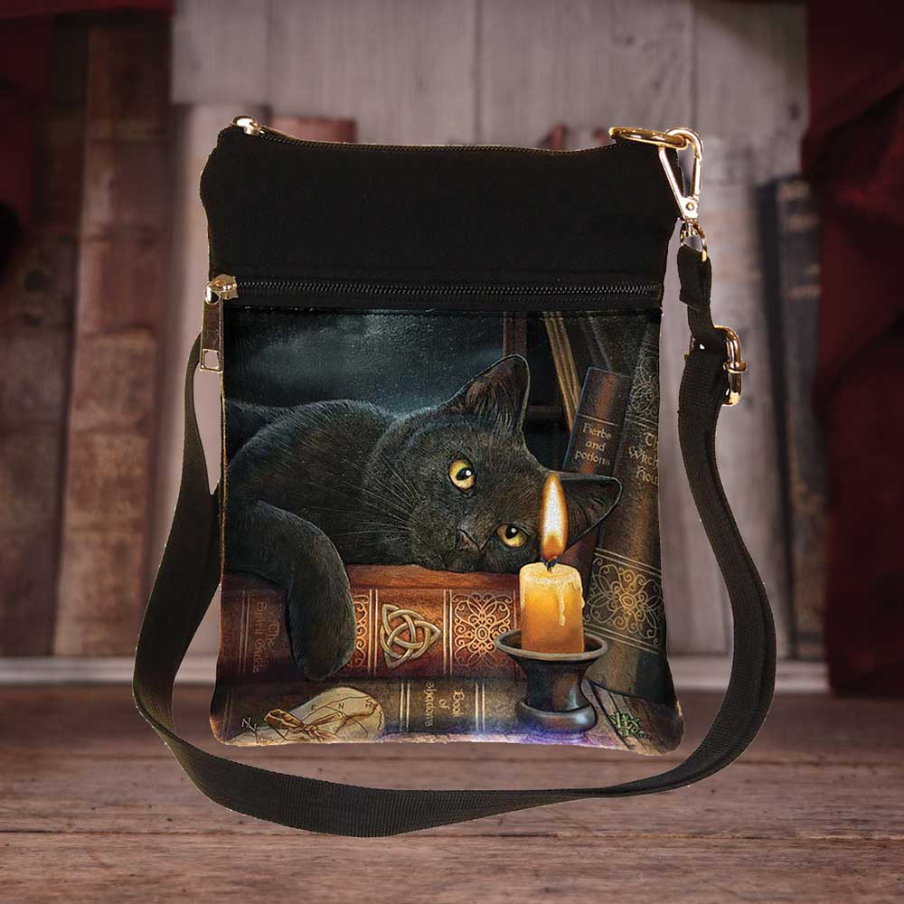A crossbody bag displays a black cat lounging atop books, near a lit candle. Book titles include “Herbs and Potions” and “The Complete Witch’s Handbook”. The bag is set against a blurred bookshelf background.
