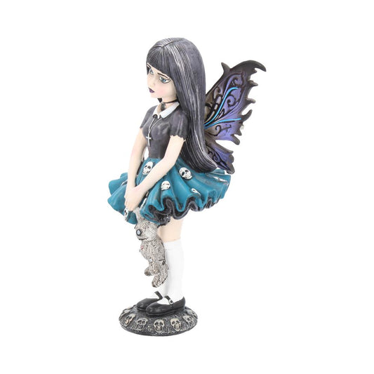 A fairy figurine stands, holding a ragged teddy bear, on a skull-covered base. It wears a black dress, a skull-printed skirt, and has purple and black filigree wings.