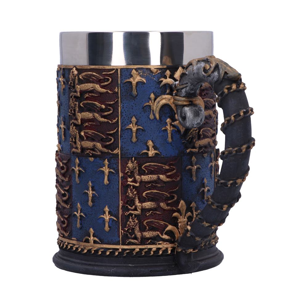 A decorative stein features a metal interior. The exterior shows a divided shield design of fleur-de-lis, and lions, with a dragon’s head atop the handle. The stein is centered against a white background.