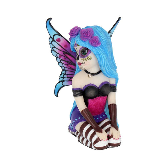 A fairy figurine kneels with colorful wings, blue hair adorned with purple roses, and Day of the Dead face paint. She's wearing a purple dress and striped stockings in a white background.