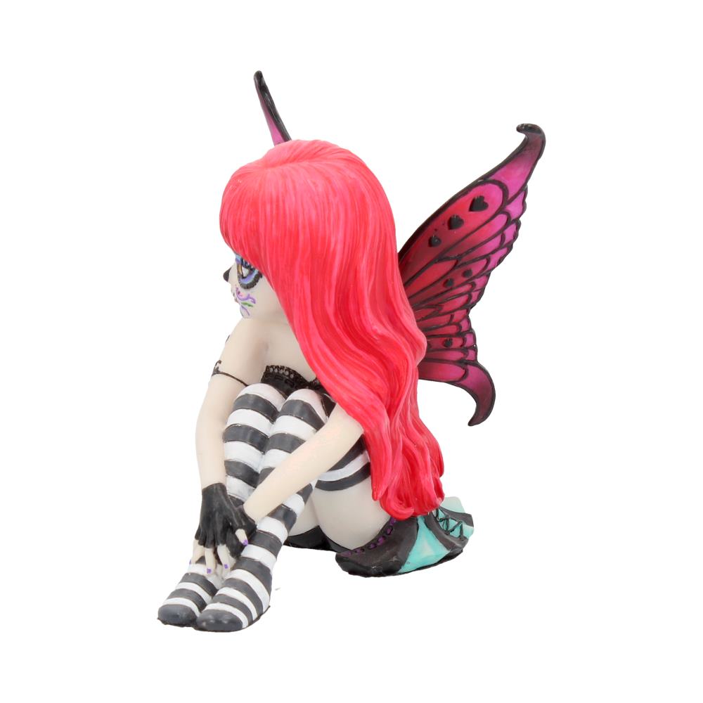 A small figurine of a fairy with red hair sits hugging her knees. She has striped stockings and pink, heart-decorated wings. The background is plain white.