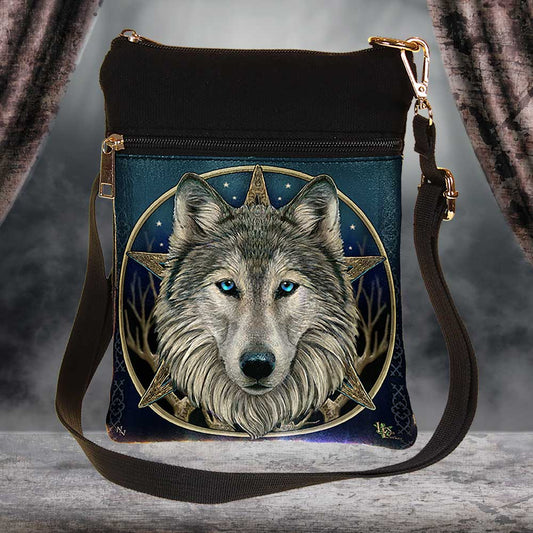 A black crossbody bag displays a wolf’s face in front of a compass star on a blue, star-studded background. The bag features a dark strap and is situated in a neutral setting with draped fabric.