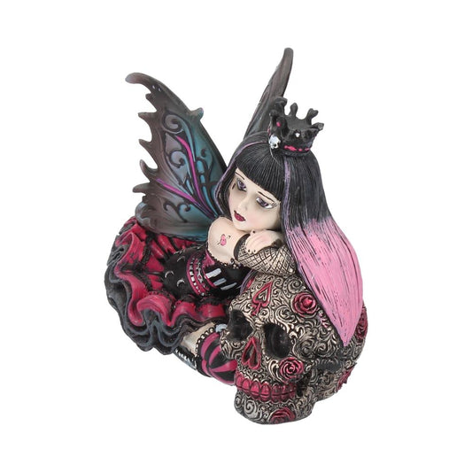 A fairy figurine with pink and black hair rests on a decorative skull adorned with red roses, featuring intricate wings and a red and black dress.