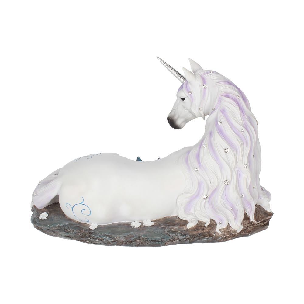 A unicorn statue lies on a brown, weathered stone base, its white and lavender mane draped over its body. Crystals are embedded in its mane and body.