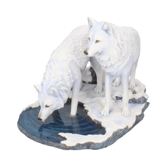 Two white wolf sculptures, one drinking from a blue water pool and the other standing alert, positioned on a snow-covered rocky base.