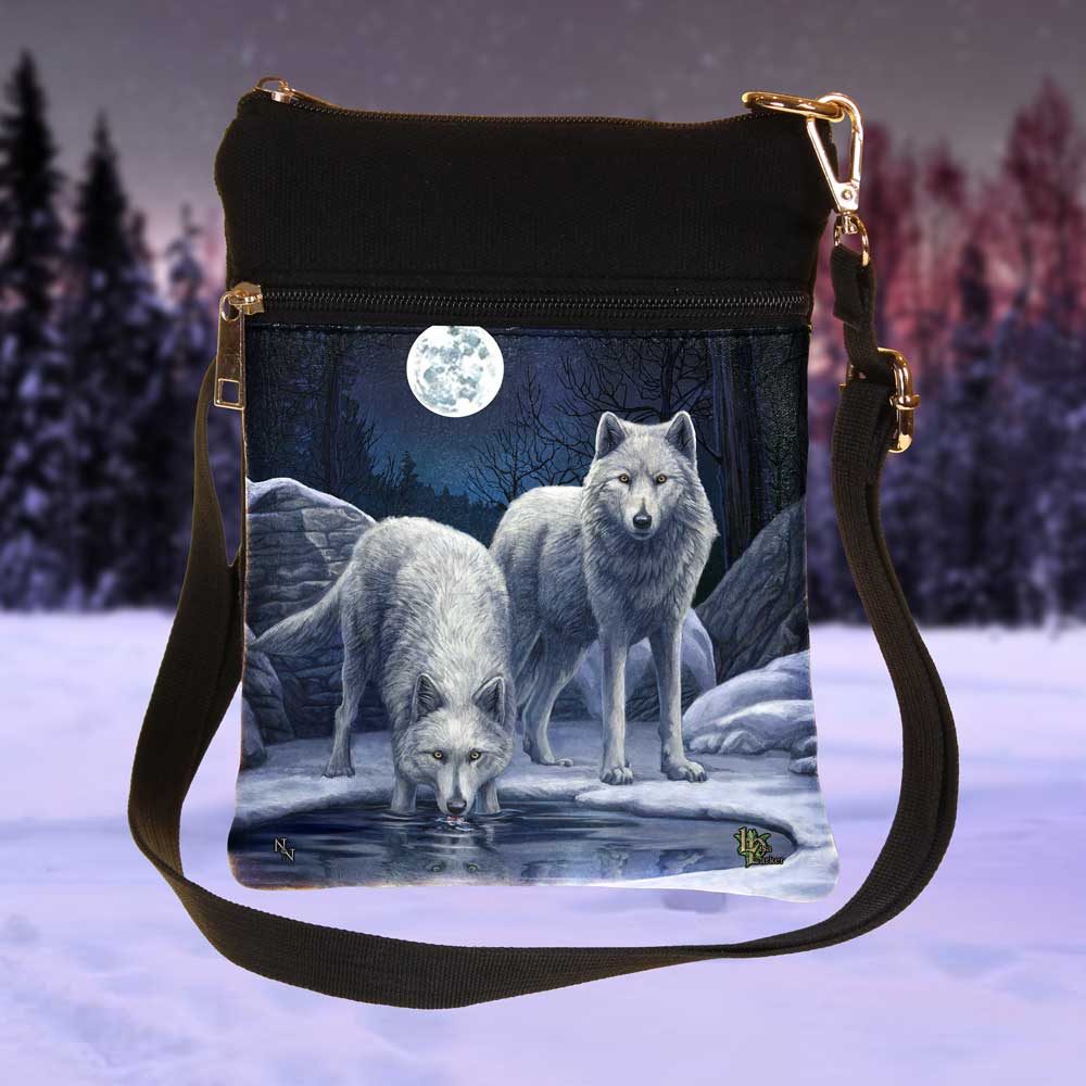A crossbody bag displays two wolves by water under a full moon and wintery sky. The top of the bag is black, with a zipper closure and shoulder strap.