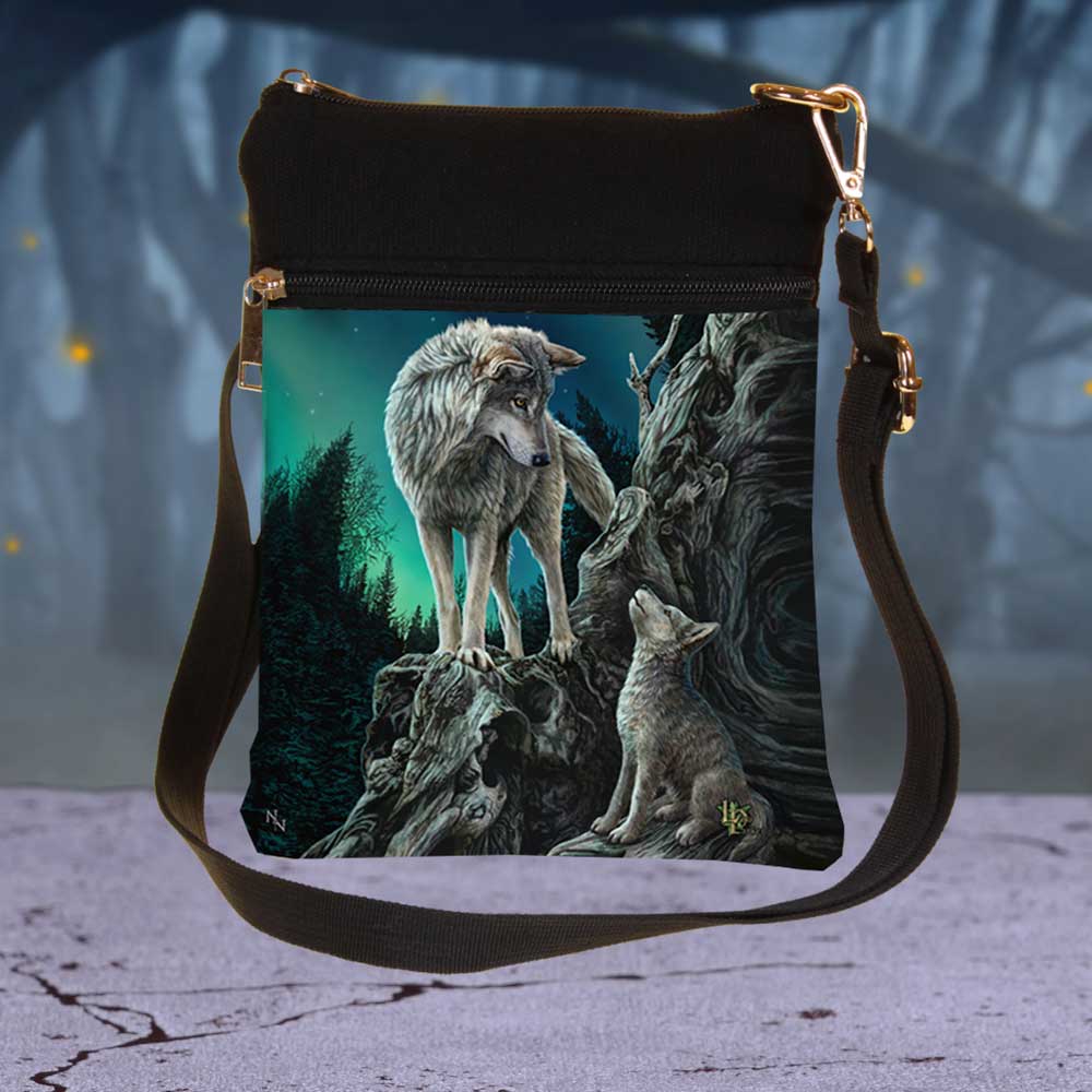 A black cross-body bag showcases a print of two wolves on a rock formation against a forest and aurora backdrop. One wolf stands, the other howls.