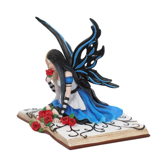 A fairy with black and blue wings kneels on an open book, smelling a red rose. Vines and additional roses decorate the pages around her.