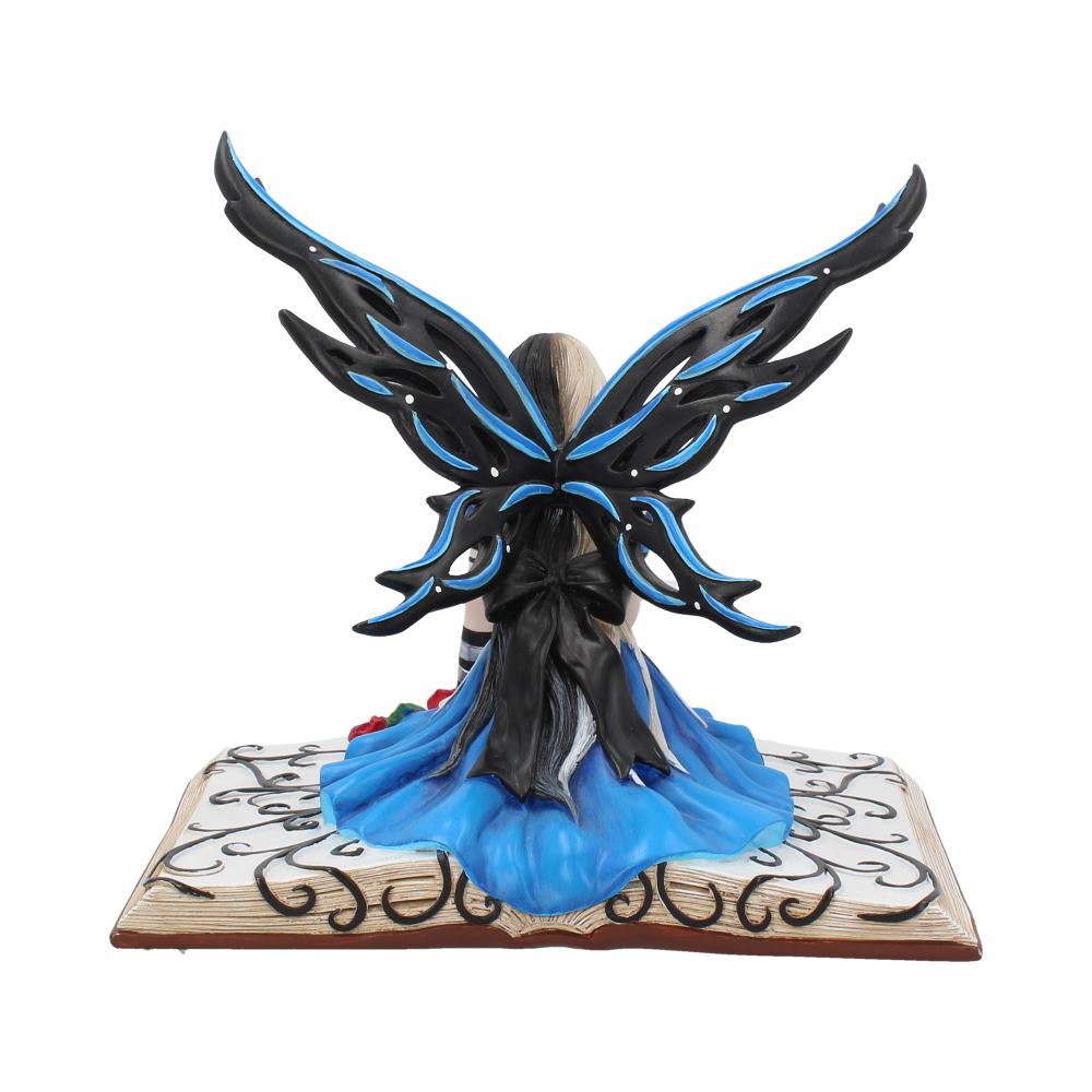 A figurine of a fairy with intricate black and blue wings sits on an open book with decorative scrolls, wearing a flowing blue dress.