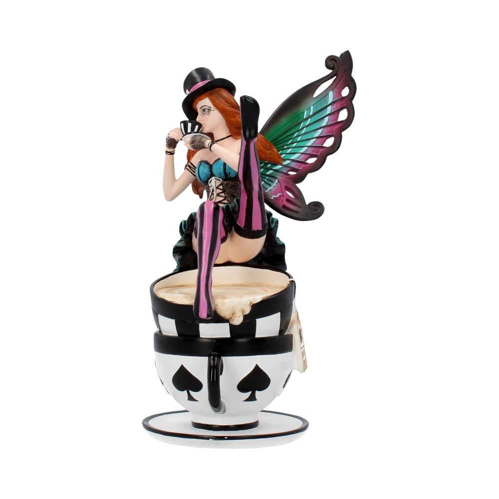 A figurine depicts a fairy with colorful wings sitting on a large, patterned teacup. She wears a top hat and corset, holding playing cards in a whimsical setting.
