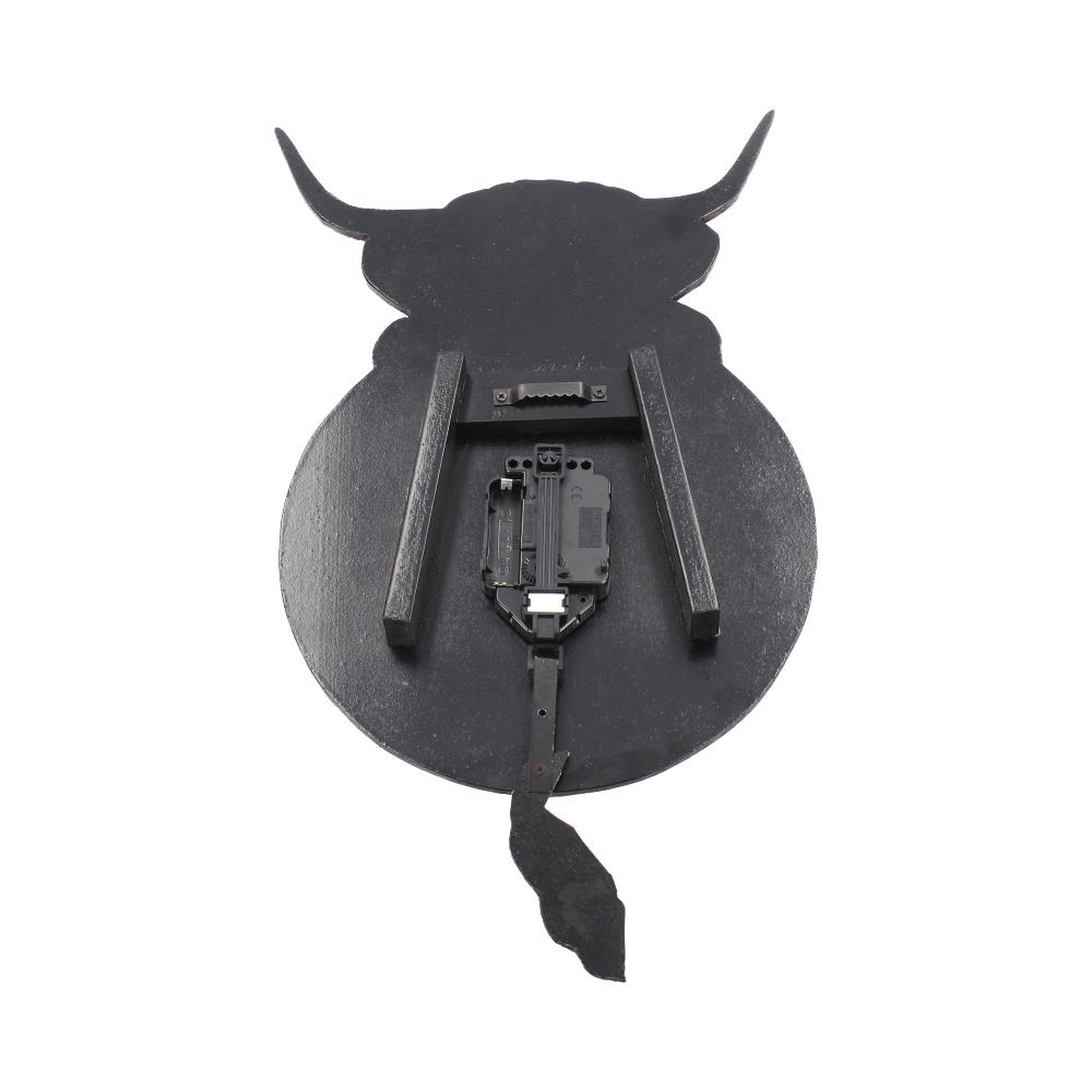 The black cow-shaped clock is seen from the back, where the clock motor and pendulum mechanism hang, with two wooden slats allowing it to be hung on a wall.
