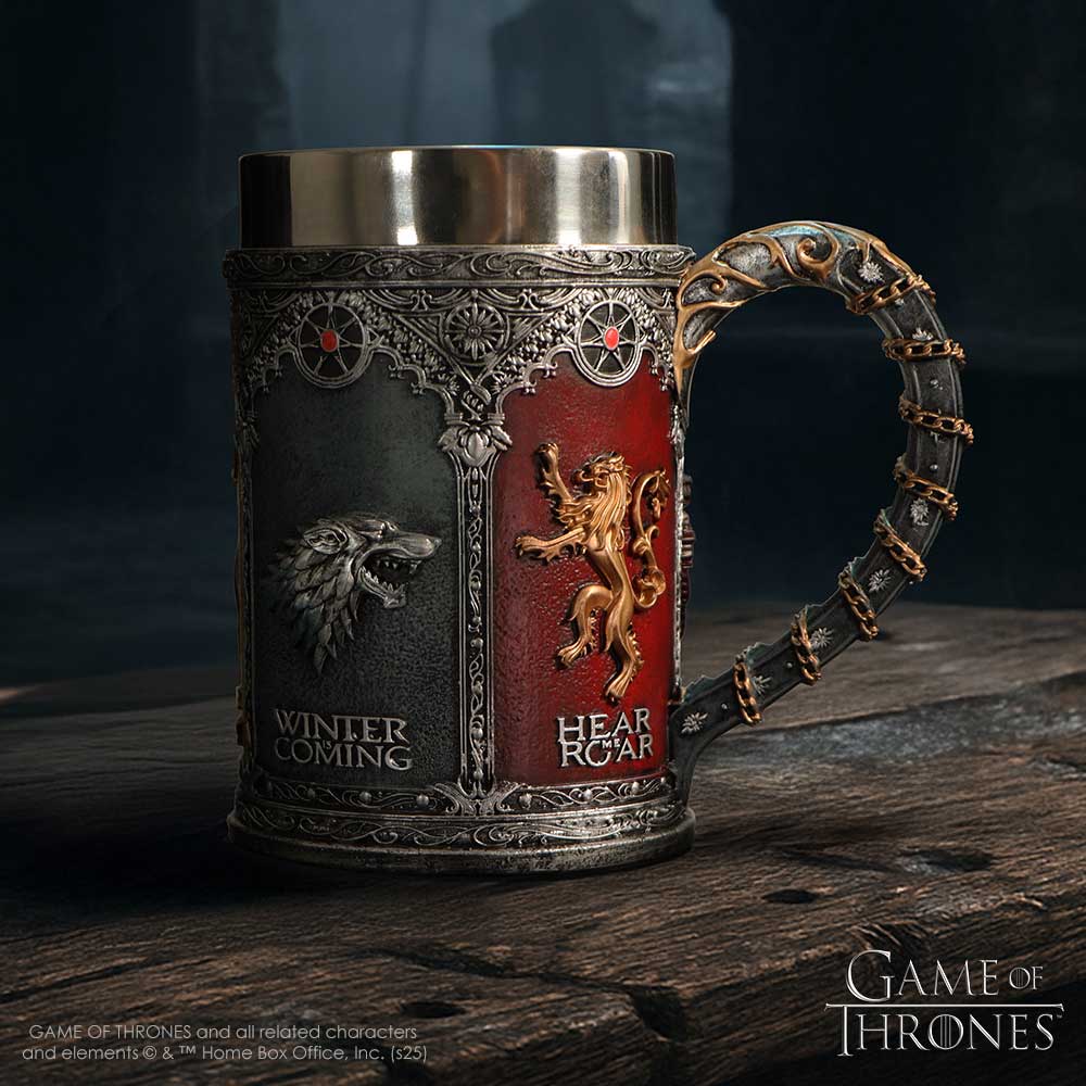 Ornate metal Game of Thrones tankard sits on a rough wooden table, displaying Stark and Lannister sigils in relief against grey and red panels in a dim medieval interior; visible text: WINTER COMING; HEAR ME ROAR; GAME OF THRONES; GAME OF THRONES and all related characters and elements © & ™ Home Box Office, Inc. (s25)