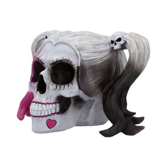 A decorative white skull with exaggerated eyelashes and painted features, including a pink heart, sports pigtails with black tips and small skull ties, on a plain background.