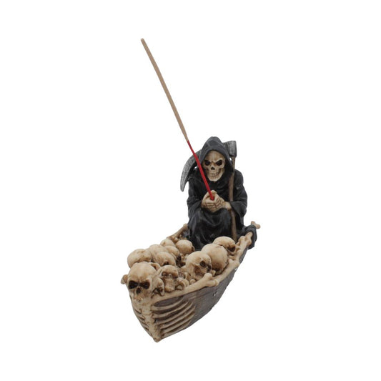 A Grim Reaper figurine sits in a skull-filled boat, holding an incense stick; isolated on a white background.