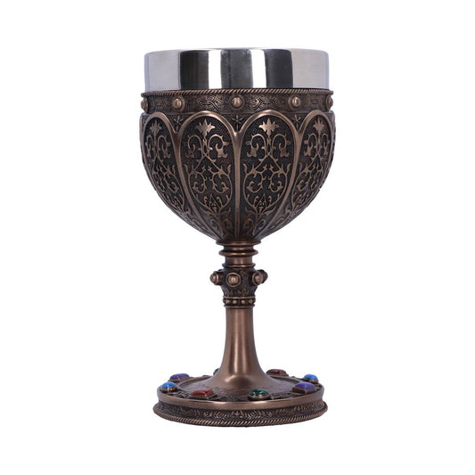 An ornate bronze chalice, trimmed with a silver top and colorful jewels at the base, sits on a white surface. The bowl features a filigree pattern.
