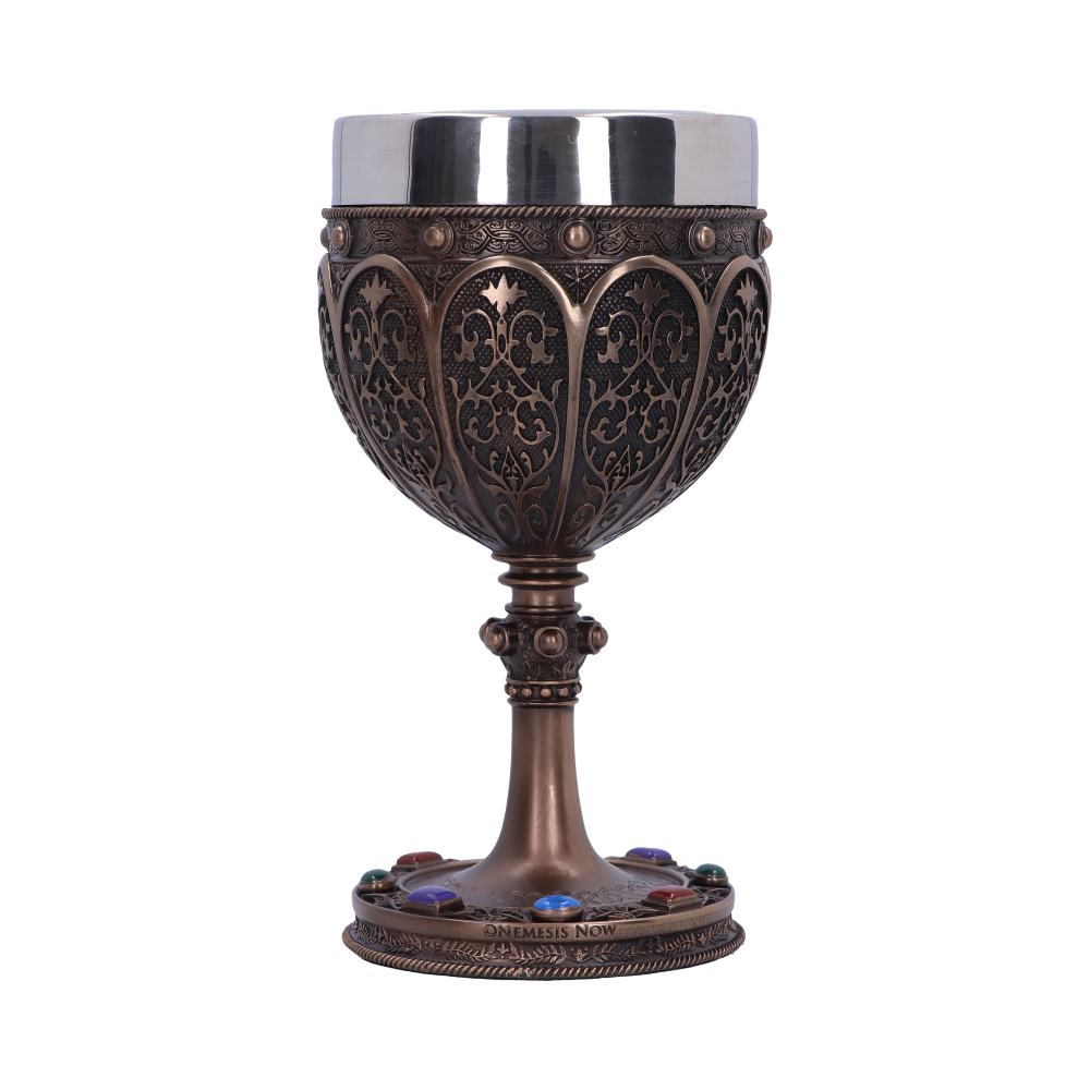 An ornate chalice with a silver top, bronze filigree bowl, and jeweled base stands on a white surface. The base is engraved with text that reads, "ONEMESIS NOW."