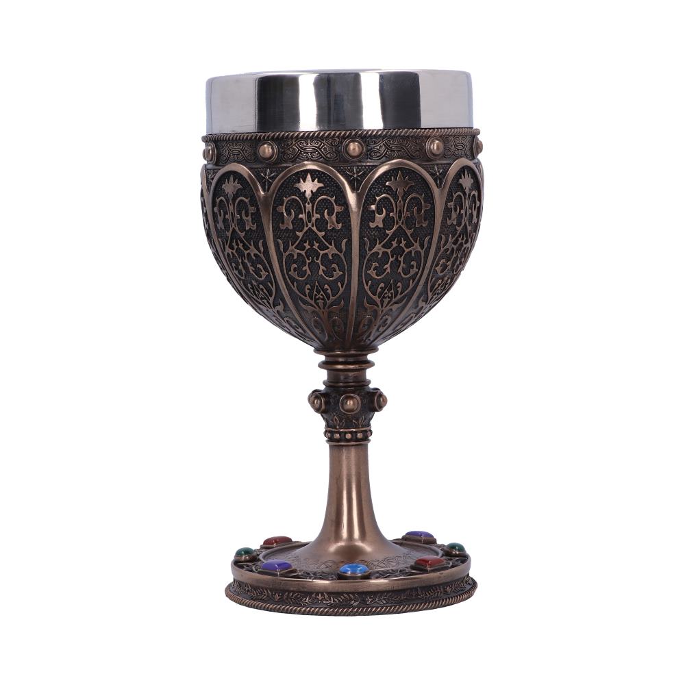An ornate, metal chalice stands upright. The cup is detailed with patterns and a silver lip. Colored gems adorn the chalice's base. The background is plain white.