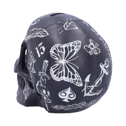 Black skull-shaped object adorned with white illustrations including a butterfly, anchor, diamond, spade, number "13," and other designs, set against a plain background.