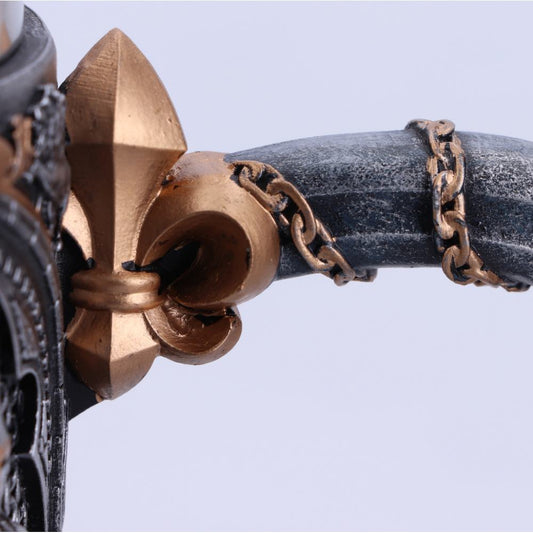A decorative sword handle features a fleur-de-lis embellishment and a chain wrapping around the grip, set against a bright, neutral background.