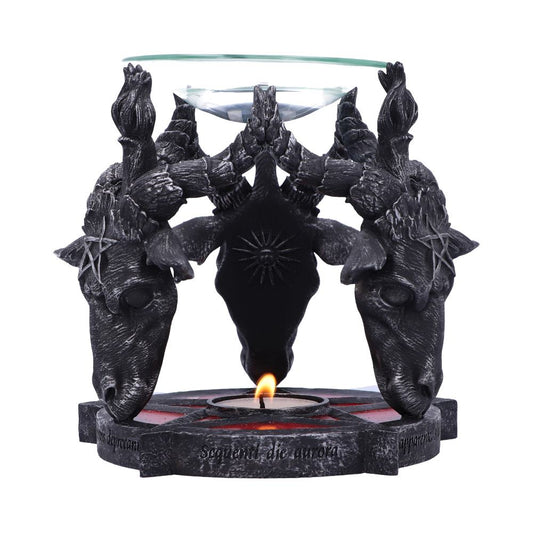 Black candle holder with three goat heads, supporting a glass dish. A lit tealight is beneath, surrounded by engraved Latin text: "superiorum inferius serpenti die aurora." Fiery accents highlight the base.