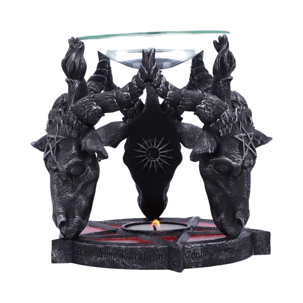 A gothic-style candle holder features three intertwined goat heads with pentagrams, supporting a glass plate. Below, a lit candle flickers. Text reads: "Et nos deum nostrim in Cordibus nostris deposuimus."