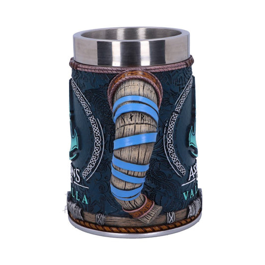 A decorative mug features a carved wooden handle resembling a horn, with blue accents. It has intricate designs and text reading "ASSASSIN'S CREED VALHALLA" on a dark, detailed exterior.