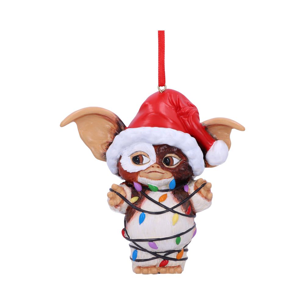 A small creature ornament, wearing a Santa hat, is wrapped in colorful Christmas lights. It hangs from a red string against a plain white background, showing festive decoration.