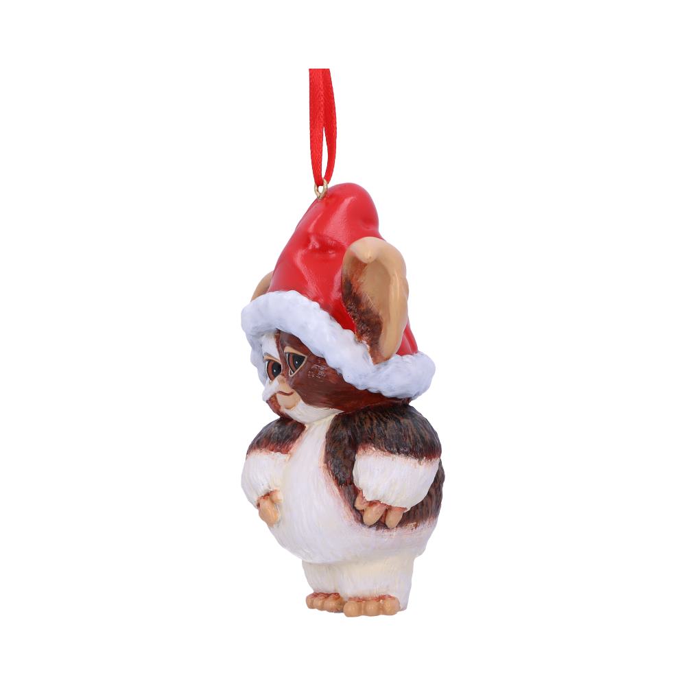 A furry, brown and white creature ornament, wearing a red Santa hat, hangs by a red ribbon, set against a plain white background.