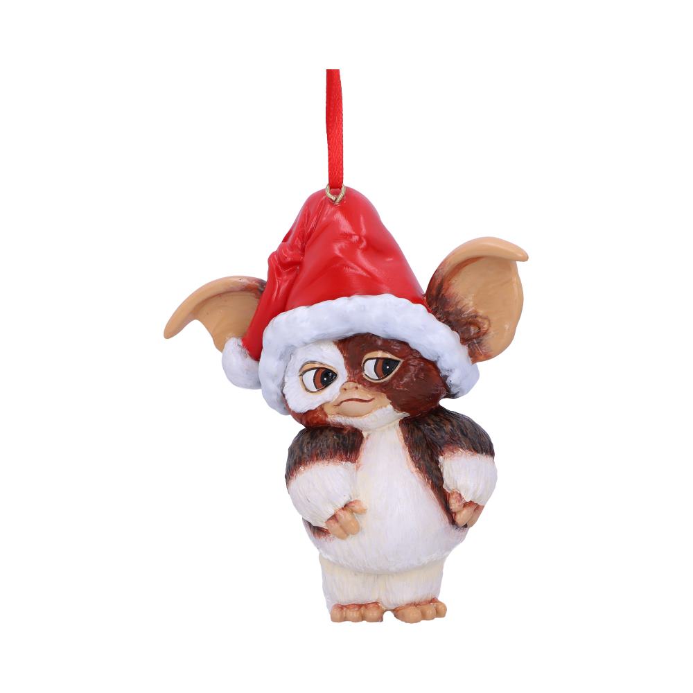 A small, furry creature ornament wears a Santa hat, suspended by a red ribbon. The creature, with large ears and expressive eyes, hangs against a plain white background.