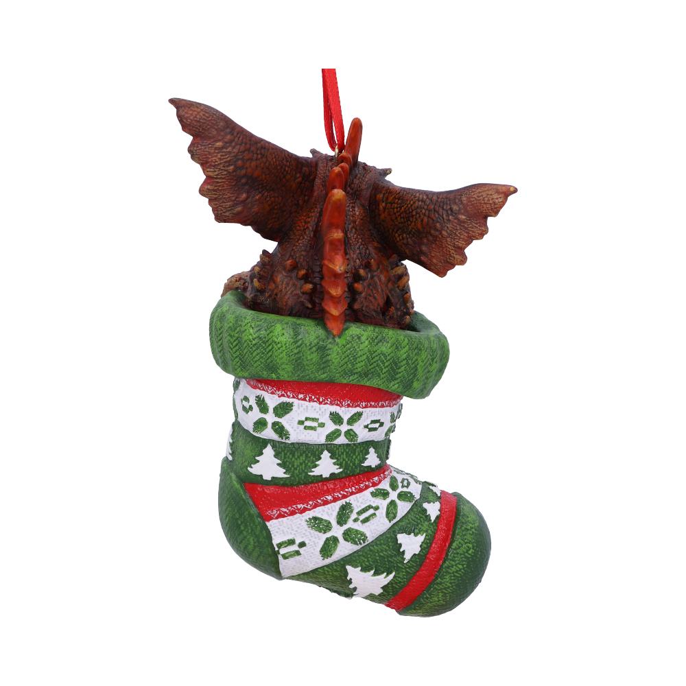 A triceratops figure is emerging from a festive green and red Christmas stocking, adorned with tree and leaf patterns, hanging by a red loop against a plain background.